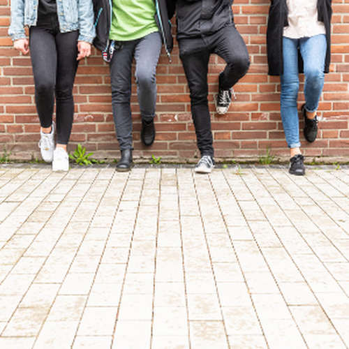Das Bild zeigt vier Jugendliche, die an einer Wand angelehnt stehen.