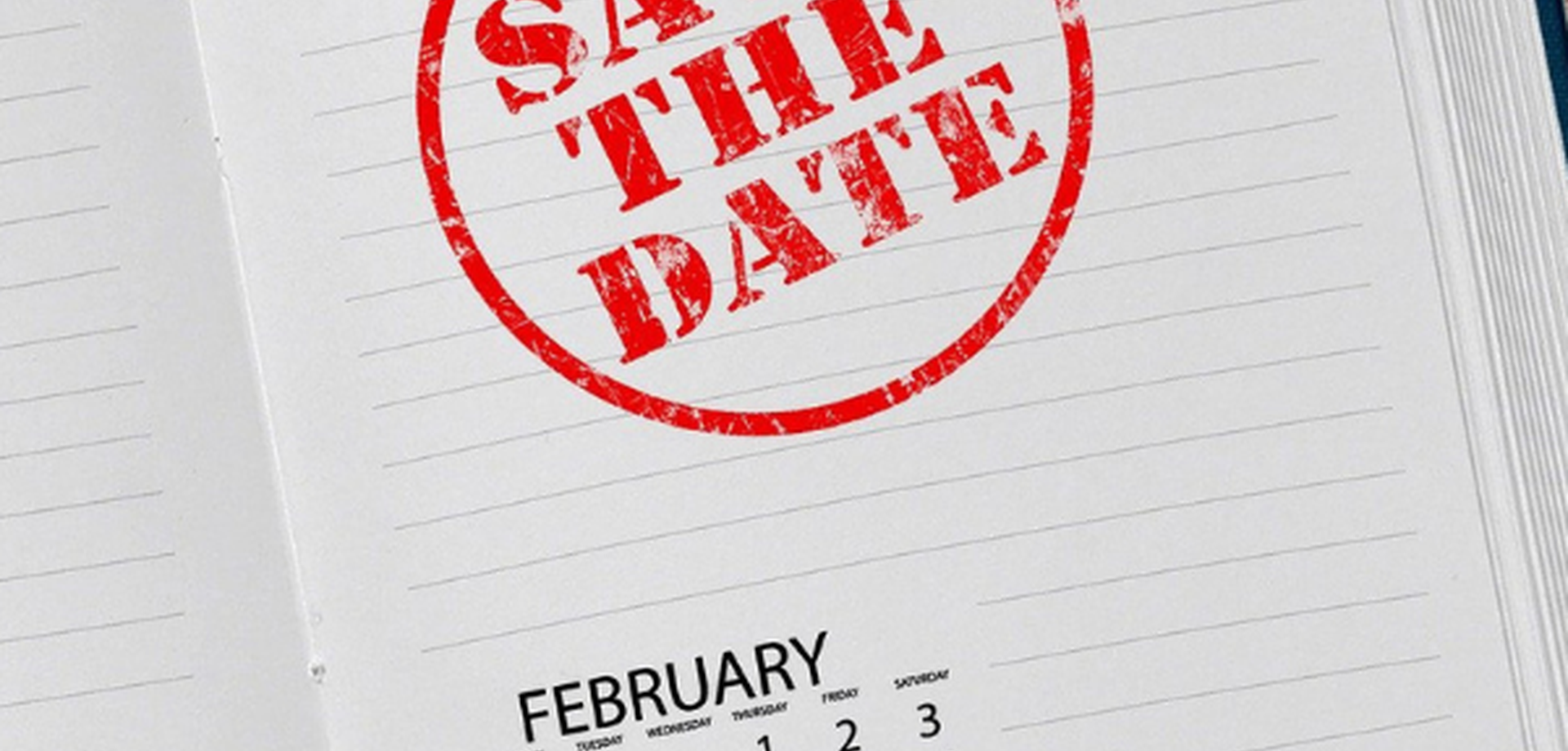 Eine weiße Seite eines Kalenderbuches ist aufgeschlagen. Dort steht in großen roten Buchstaben, umgeben von einem roten runden Kreis "Save the Date"