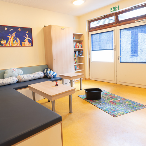 Das Bild zeigt einen Wohnraum mit einer schwarzen Couch und einem hellen Bücherregal.