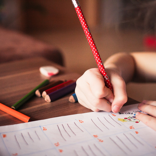Das Bild zeigt ein Mädchen, das mit einem Stift etwas auf ein Blatt Papier schreibt.