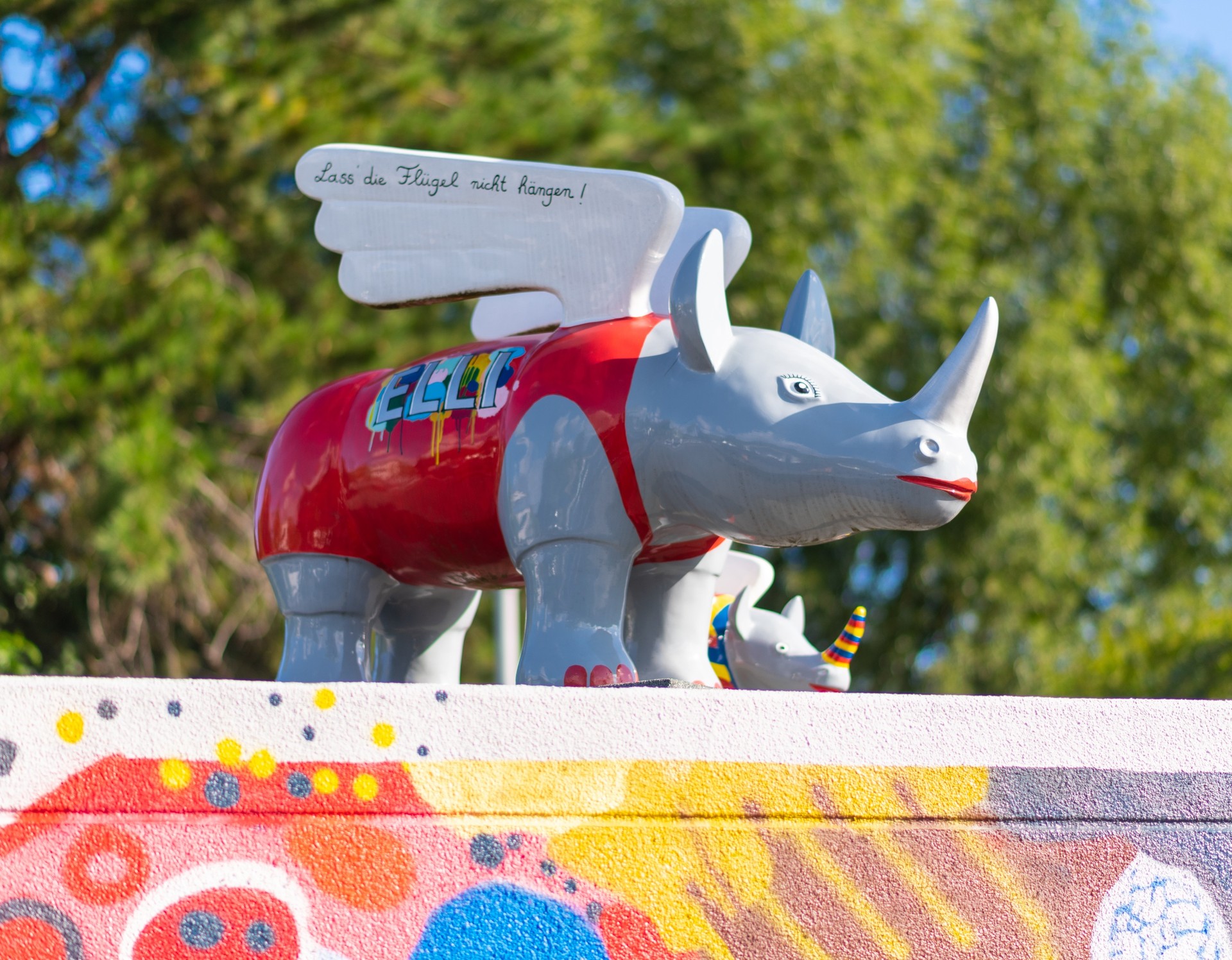 Das Bild zeigt zwei kleine, kunterbunte Nashorn-Figuren, die auf einem Dach stehen.