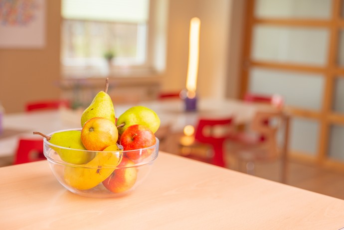Eine gläserne Obstschale mit Äpfeln, Birnen und Bananen steht auf einem Tisch.